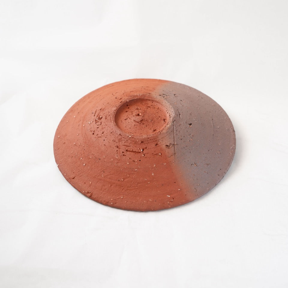 Reverse view of a unique yakishime plate by Kai Tsujimura, revealing a striking two-tone surface divided into warm terracotta red and dark ash grey by kiln transformation.