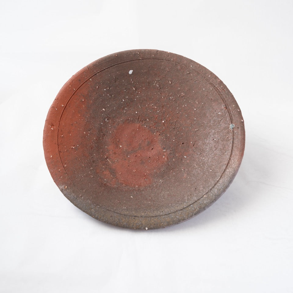 Front view of a dark brown yakishime plate by Kai Tsujimura, featuring a soft reddish fire mark captured in the center within a refined incised ring.