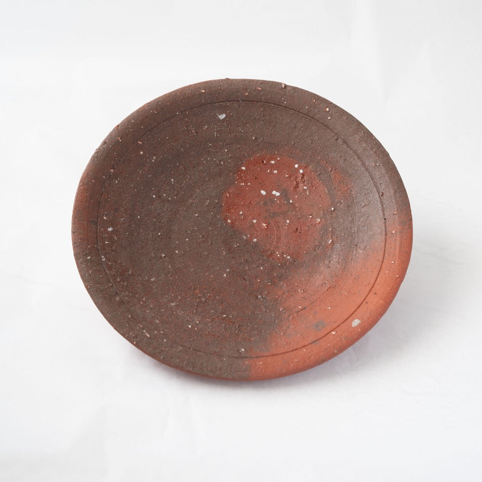 Front view of a reddish-brown yakishime plate by Kai Tsujimura, featuring a vivid orange circular fire mark and fine feldspar inclusions.