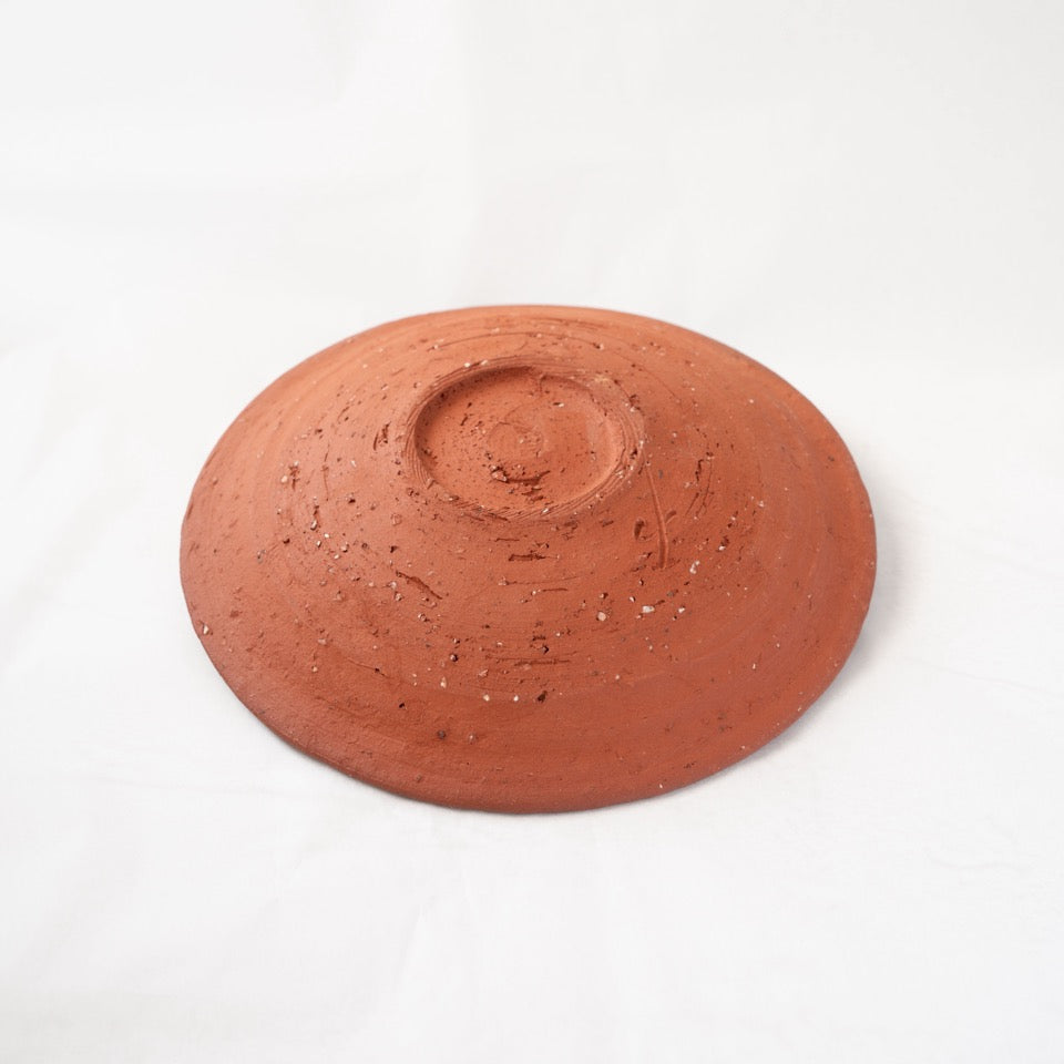 Reverse view of a warm reddish yakishime plate by Kai Tsujimura, showcasing a hand-carved foot, natural feldspar particles, and concentric textures on the unglazed ceramics surface.