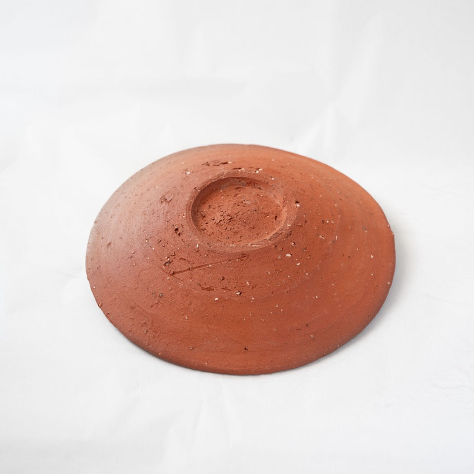Reverse view of a terracotta-red yakishime plate by Kai Tsujimura, showing the clean circular form and raw, unglazed bottom texture.