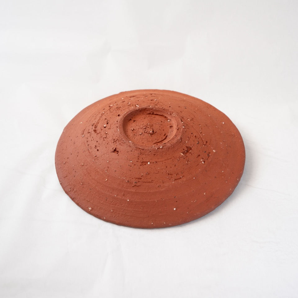 Reverse view of a warm red yakishime plate by Kai Tsujimura, detailing the fine throwing lines and coarse mineral particles on the base.