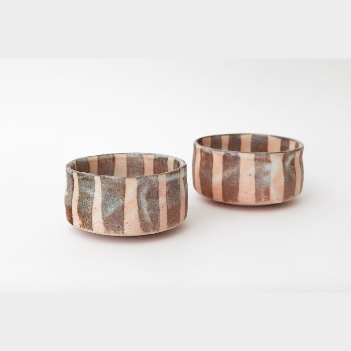 Two of the striped Shino dishes side by side on a pale ground, the rust-brown vertical bands under the white glaze; sold as a set of four.