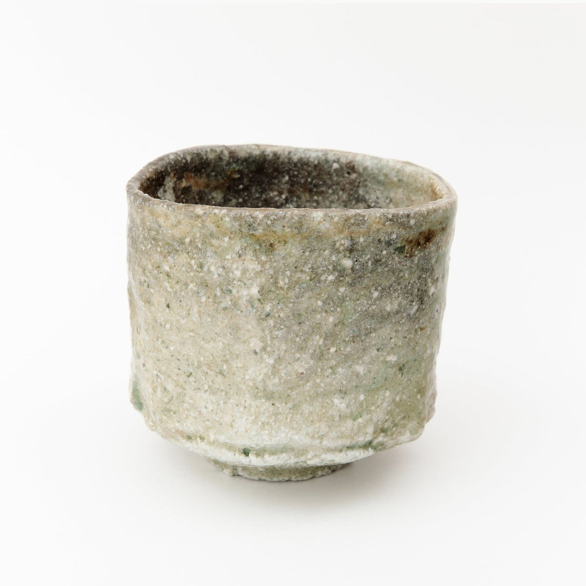 Front view of the tall Shigaraki tea bowl on a white ground, the grey-green ash surface and pale feldspar grit visible.