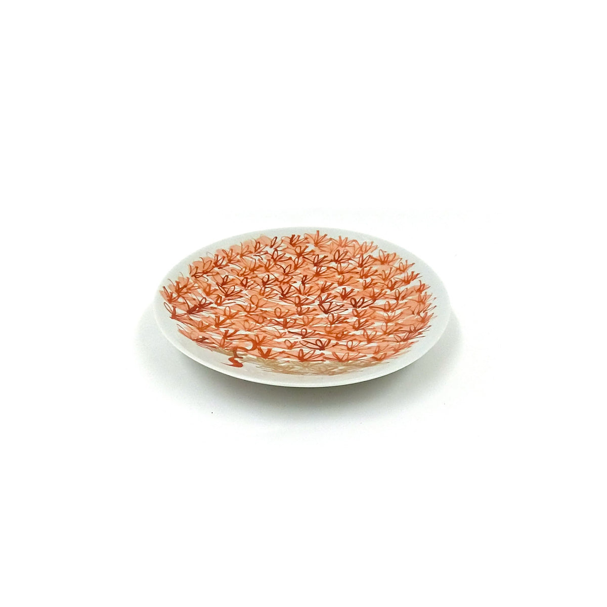 Three-quarter view of the small round plate on a white ground, densely painted with small red enamel flowers.
