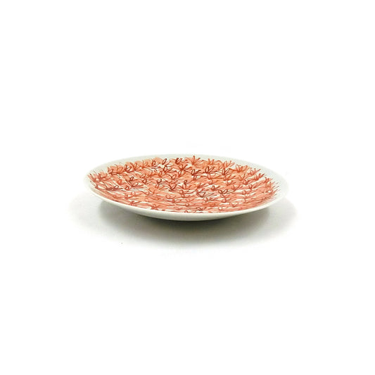 Vue de profil de l'assiette montrant son faible galbe et les fleurs rouges courant jusqu'à la lèvre.