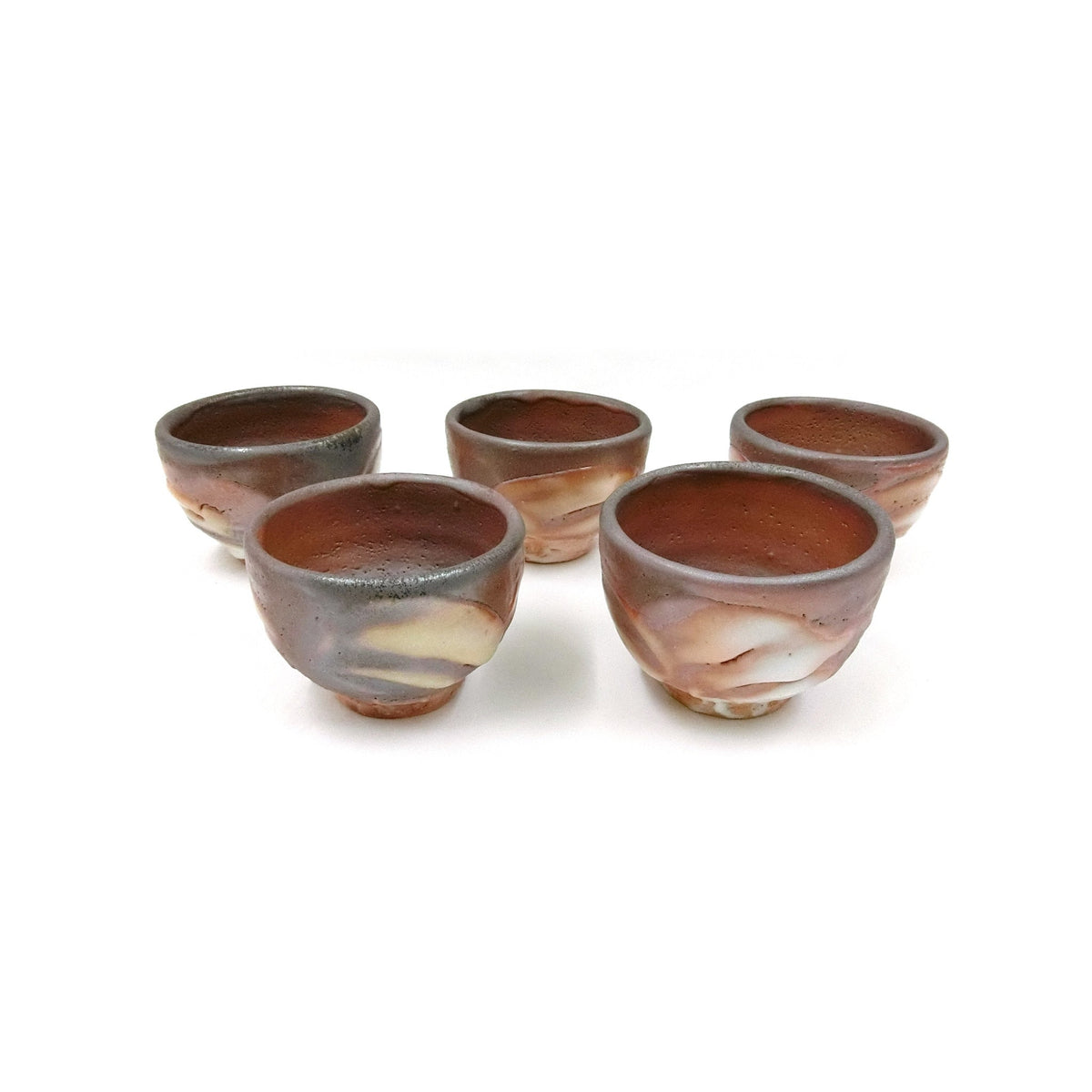 The five yohen Shino cups grouped on a white ground, each in a different mix of orange, rust and grey.