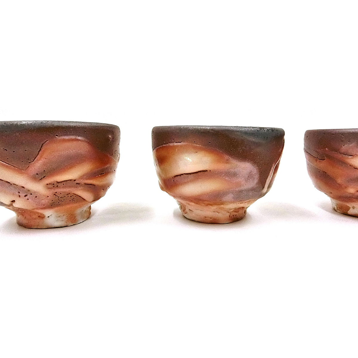 Three cups in close side view showing the flame-flashed orange and rust surfaces and grey streaks.
