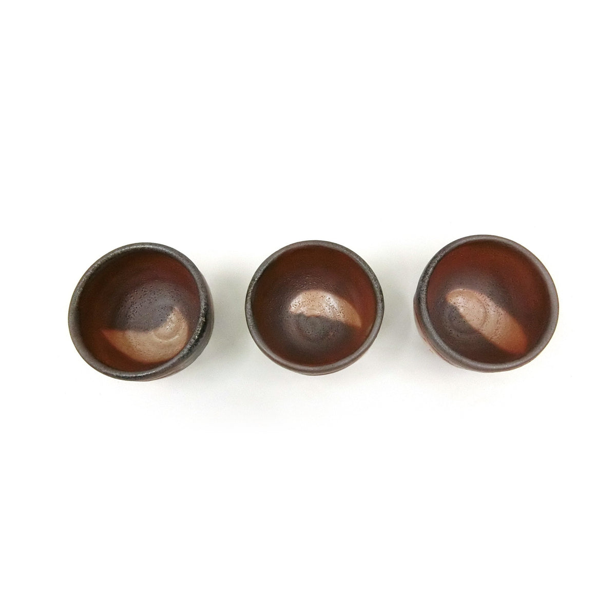 Three cups seen from above, the glaze pooling in the wells in dark brown and grey.