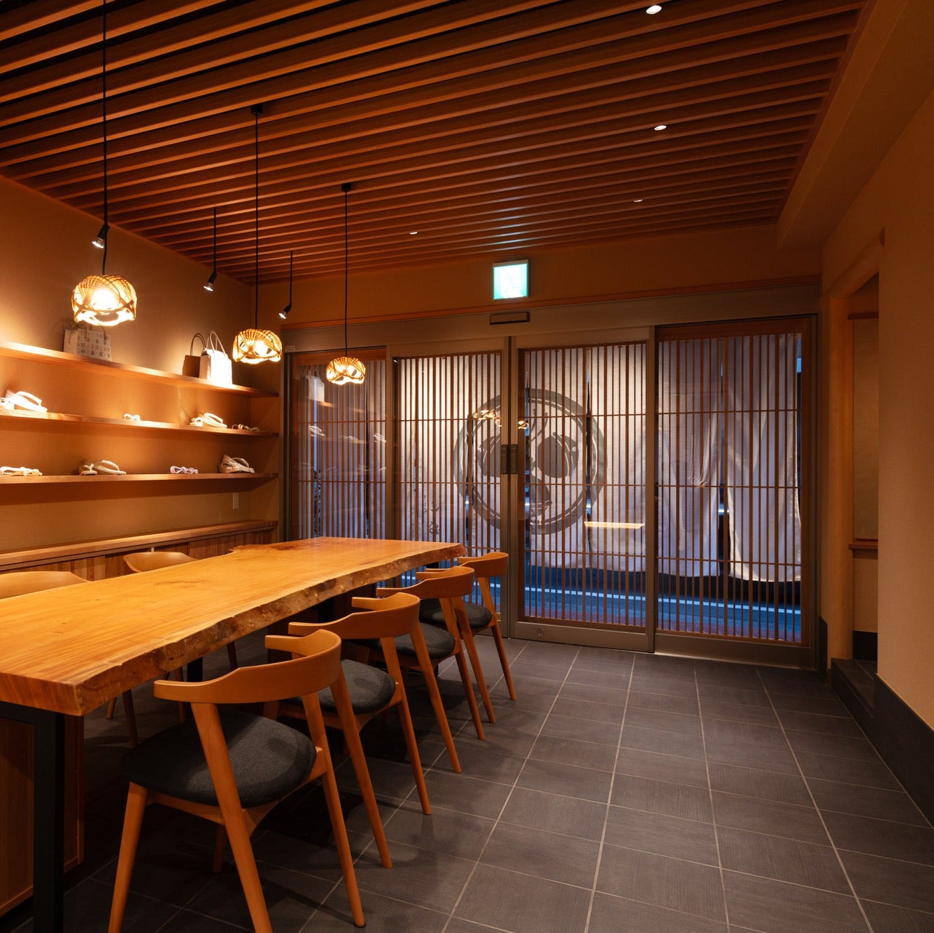 Entrance glowing at dusk beyond a live-edge counter, a serene work of Japanese architecture