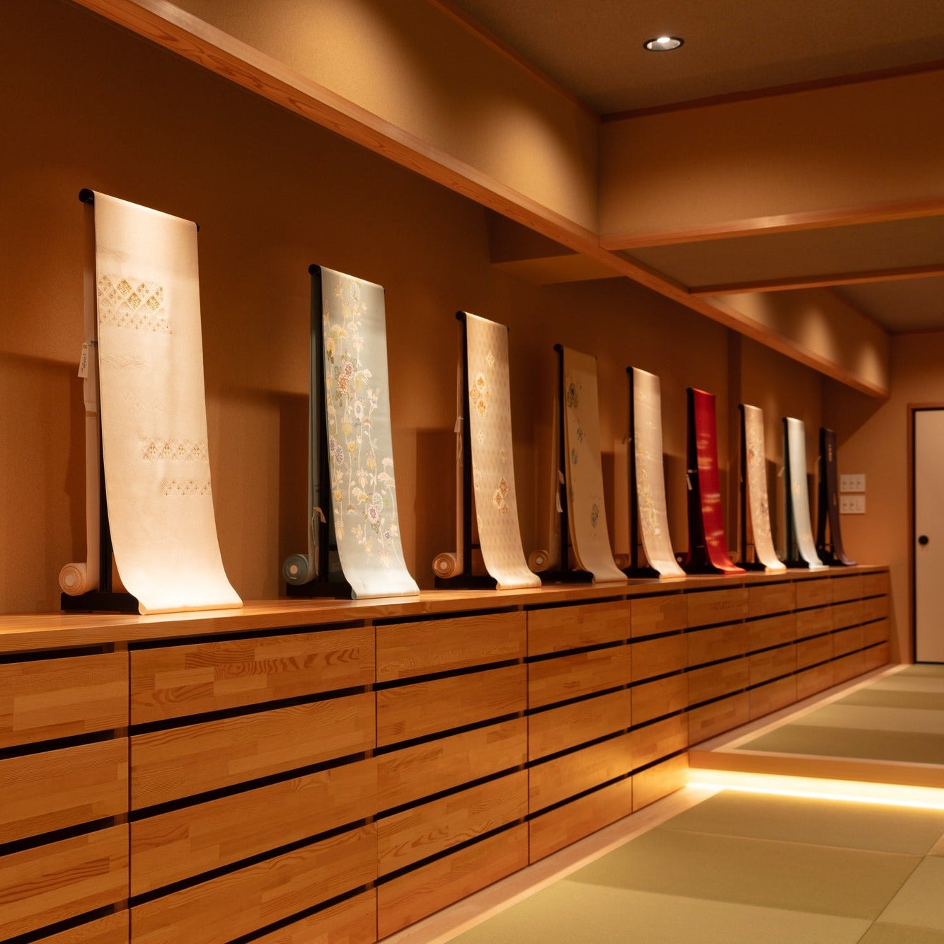 Row of obi sashes lit on black stands along a cedar chest, fine Japanese architecture joinery