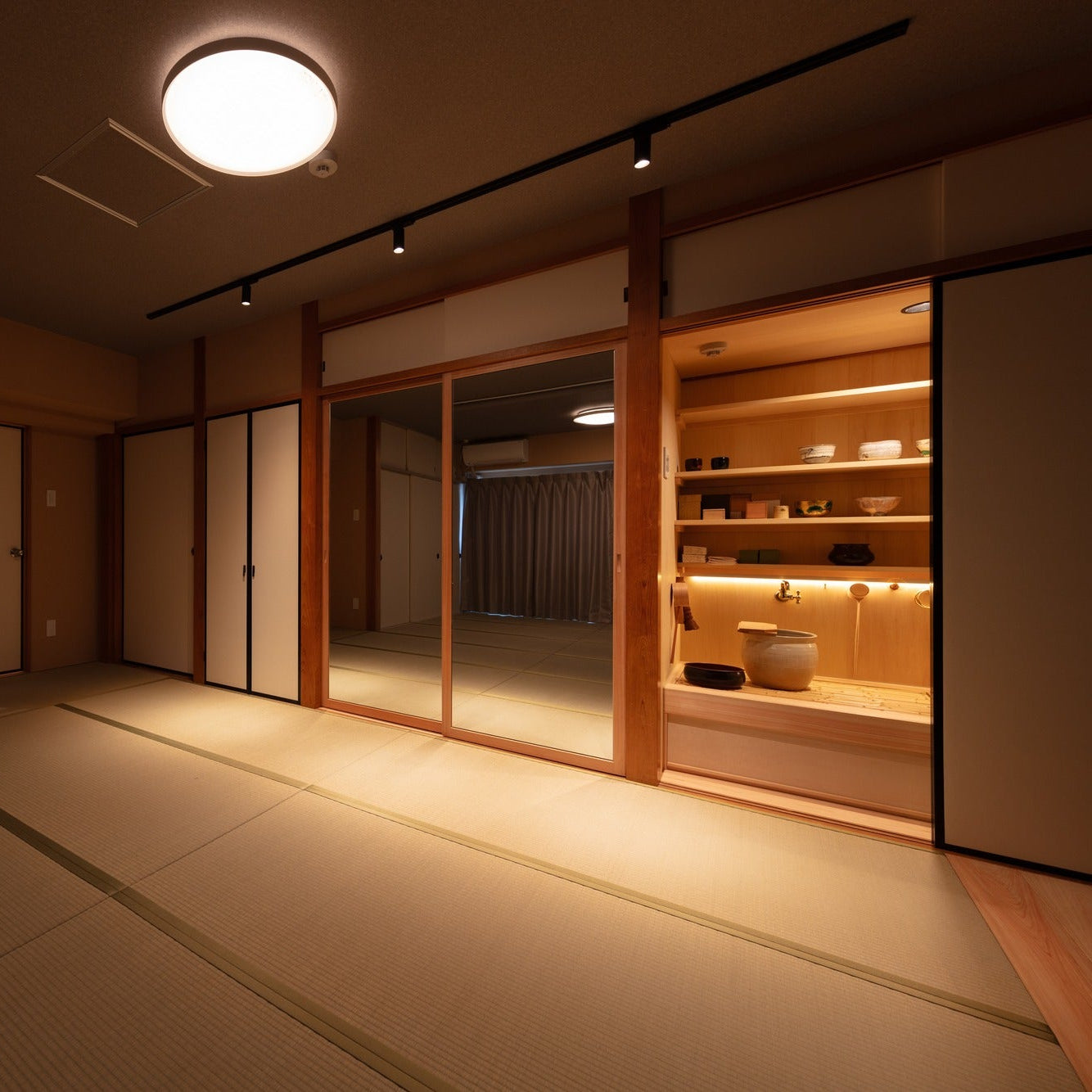 Tatami guest room at night with a lit display alcove of ceramics and a water basin