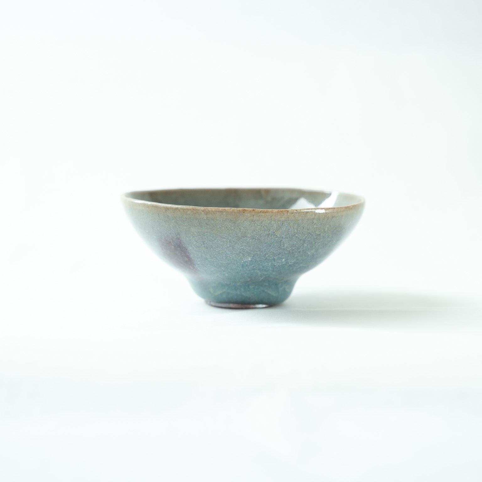 Front view of the Choyo-yu Jun-style glaze SAKAZUKI by Kiyoshi Hara, featuring a soft blue-green surface with a subtle purple-red splash on the left.