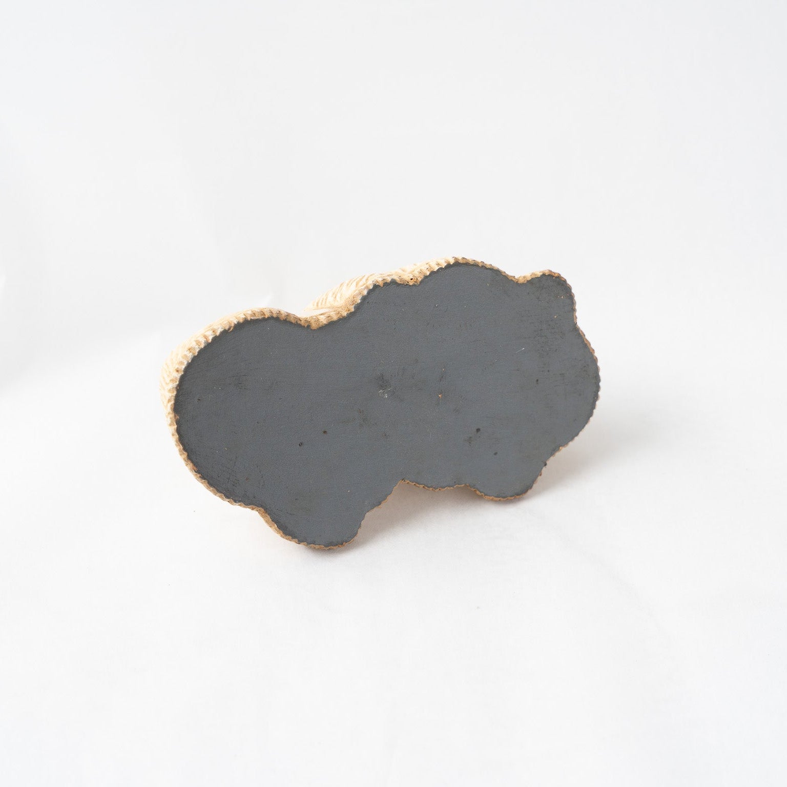 View of the flat, dark grey finished underside of the leather poodle paperweight, illustrating the seamless edge alignment of the molded leather technique.