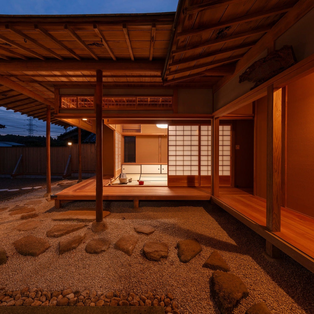 Tea house glowing at dusk above a dry garden, the chashitsu seen at blue hour