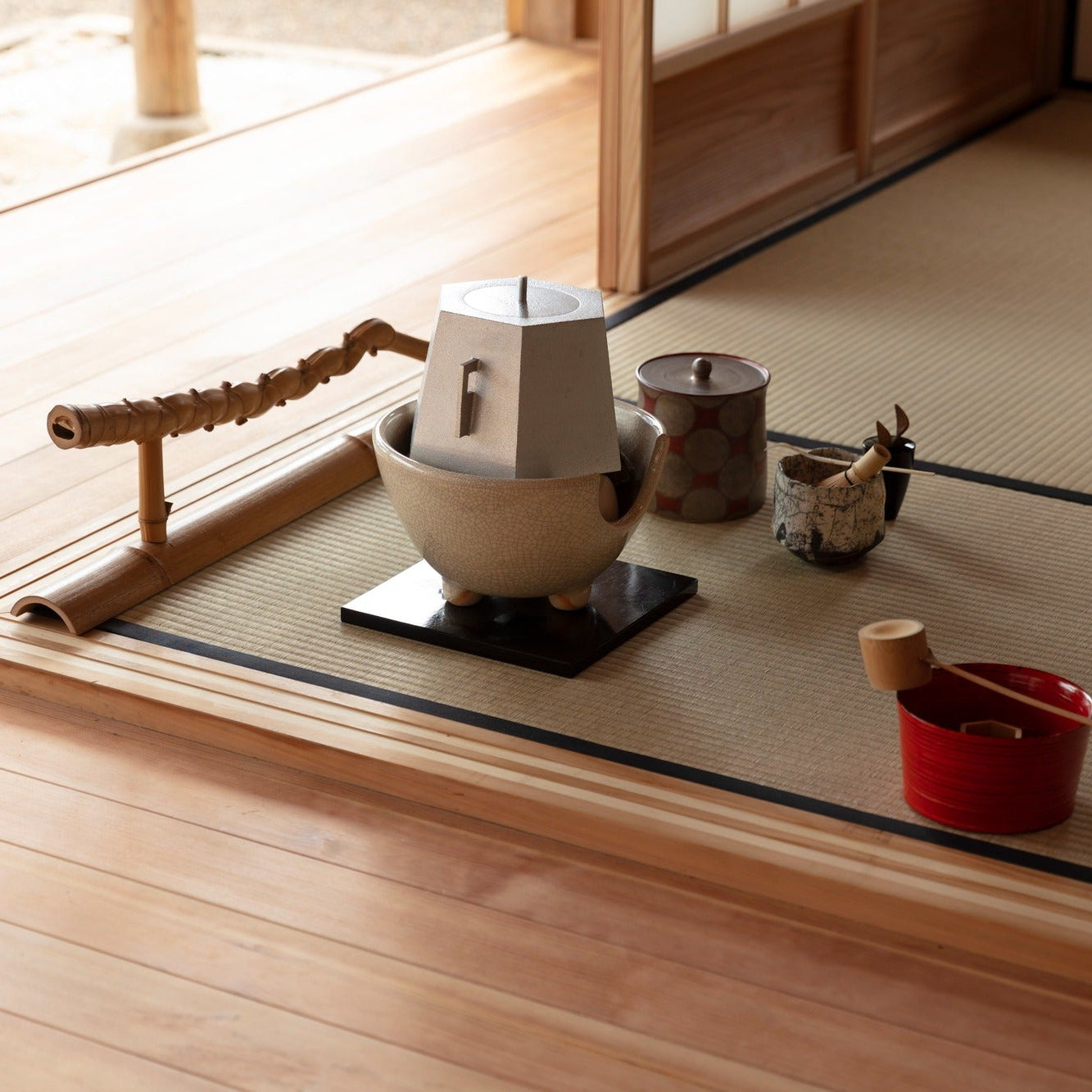 Tea utensils - a ceramic brazier, water jar, bamboo ladle and tea bowl - arranged in sunlight