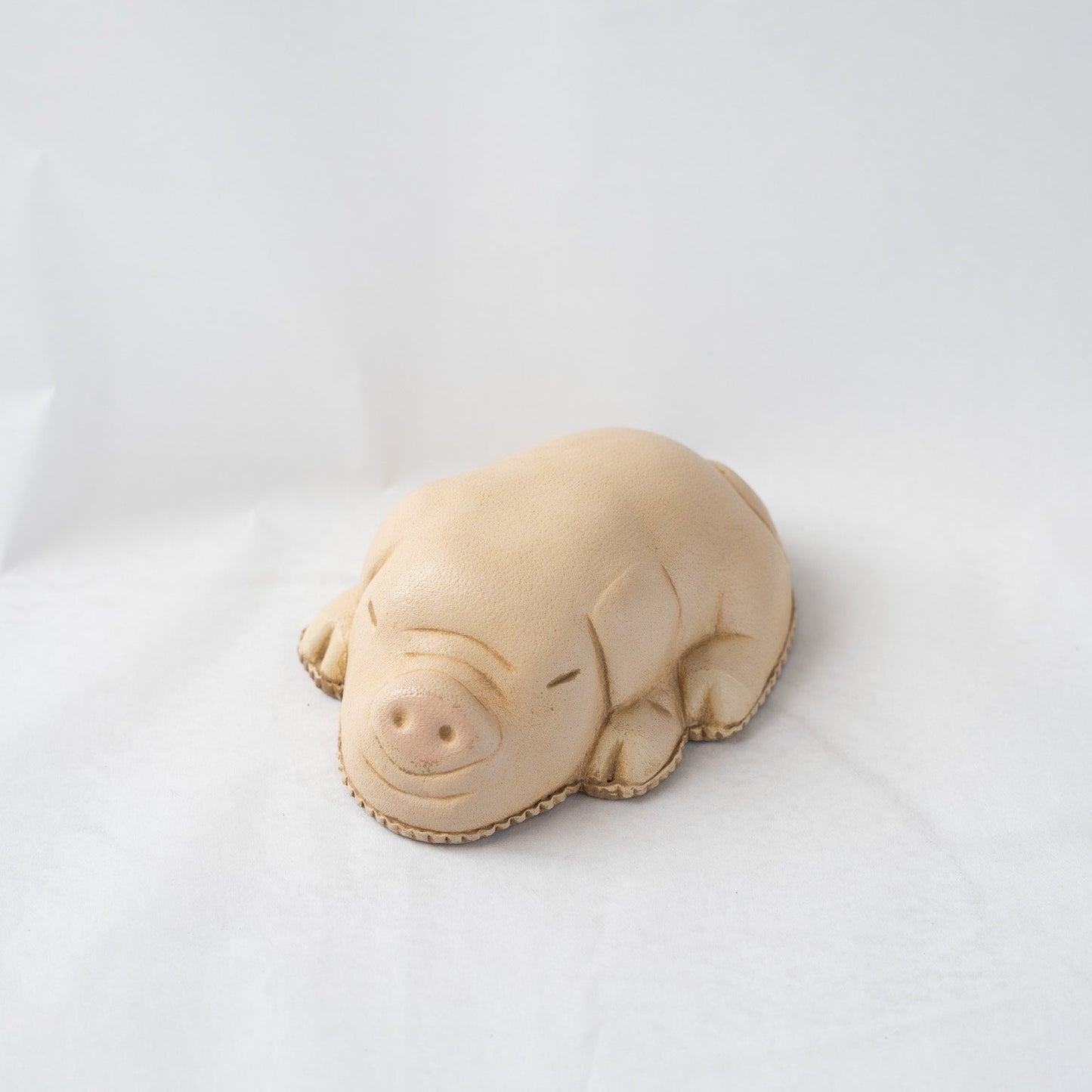 ront angled view of a sleeping pig leather paperweight by Koh Kono, highlighting the prominent molded snout, closed eyes, and smooth beige leather texture.