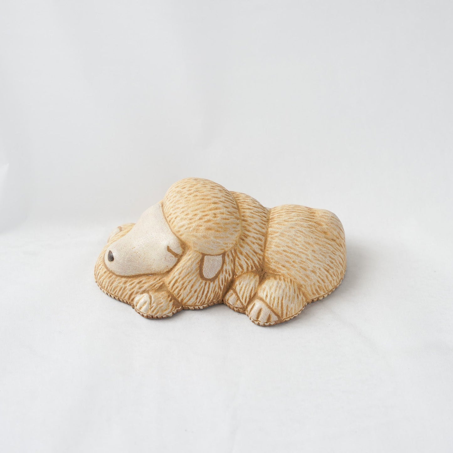 Side profile view of a sleeping poodle leather paperweight by Koh Kono, showing detailed hand-carved fur textures and natural beige leather tones.