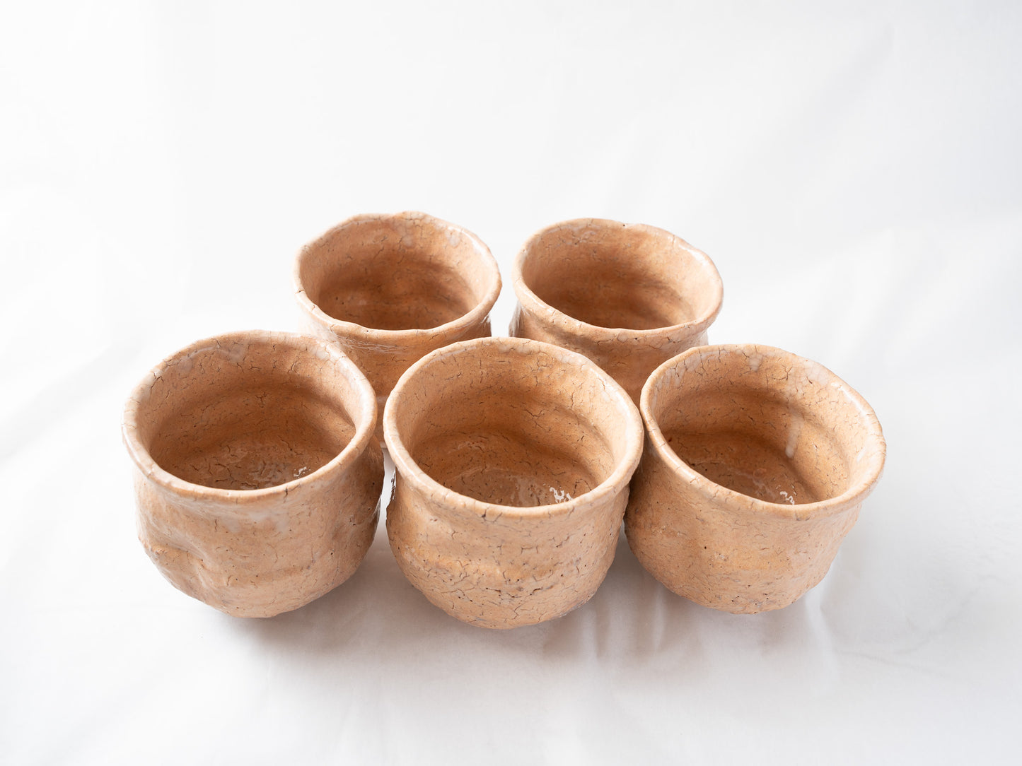 Alternate front angle of the five loquat-colored ceramic cups, highlighting the subtle differences in glaze density and firing character among each piece.
