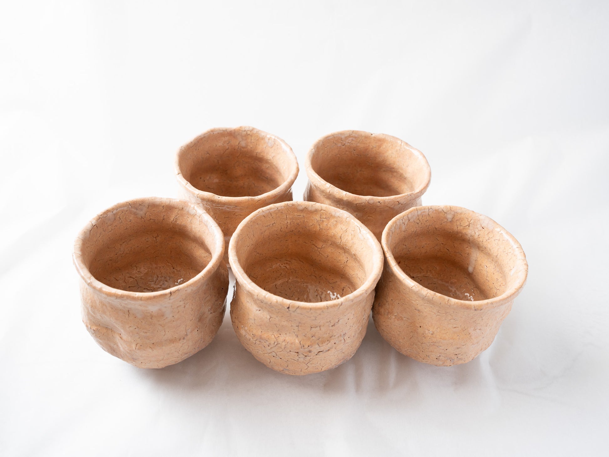 Alternate front angle of the five loquat-colored ceramic cups, highlighting the subtle differences in glaze density and firing character among each piece.