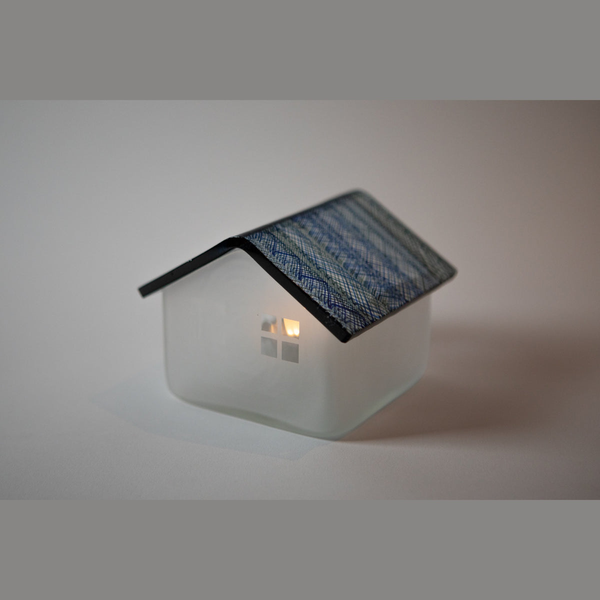The house lit from within in a darkened setting, the translucent walls glowing warm beneath the blue roof.