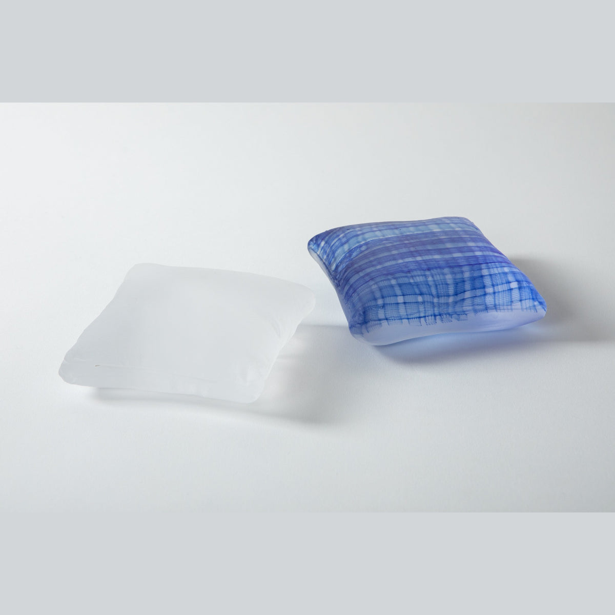 The two glass pillows side by side on a pale ground, the indigo checked pillow in front and the frosted white one behind.