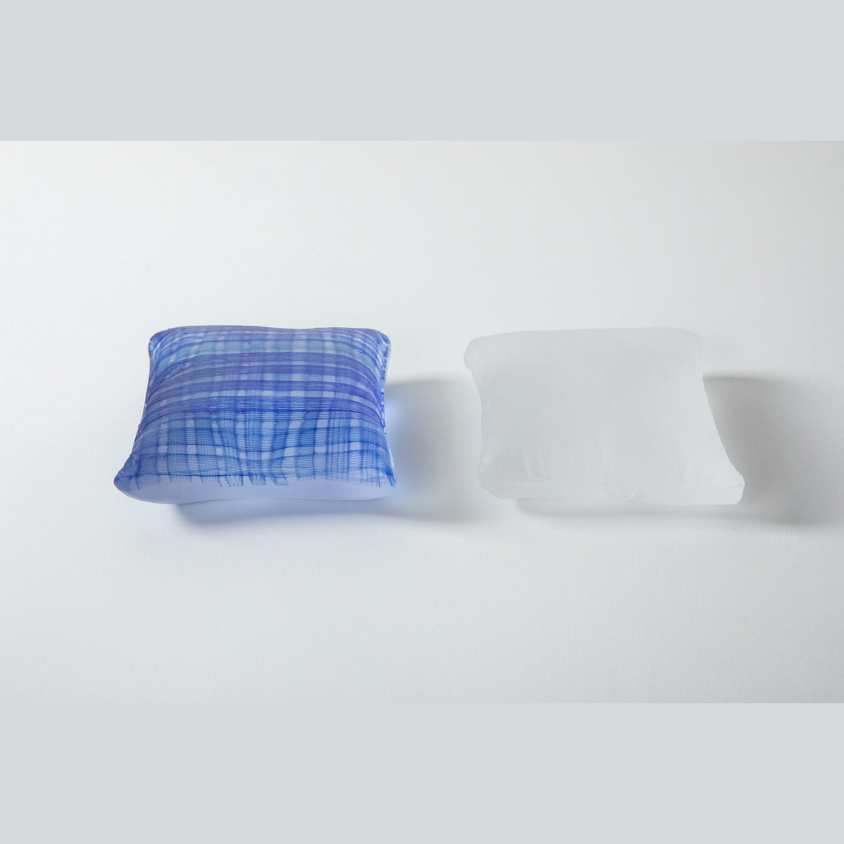 The pair viewed from the front, indigo on the left and white on the right, showing the puffed centres and dimpled corners.