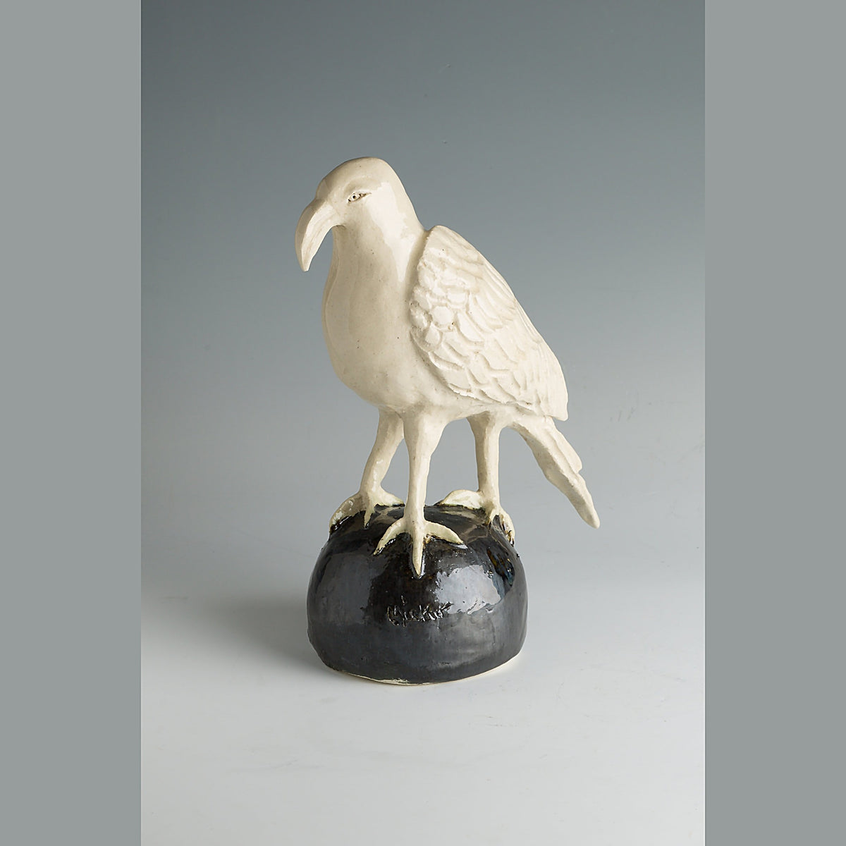 Three-quarter view of the crow with its head turned and beak lowered, incised feathers visible on the wing.