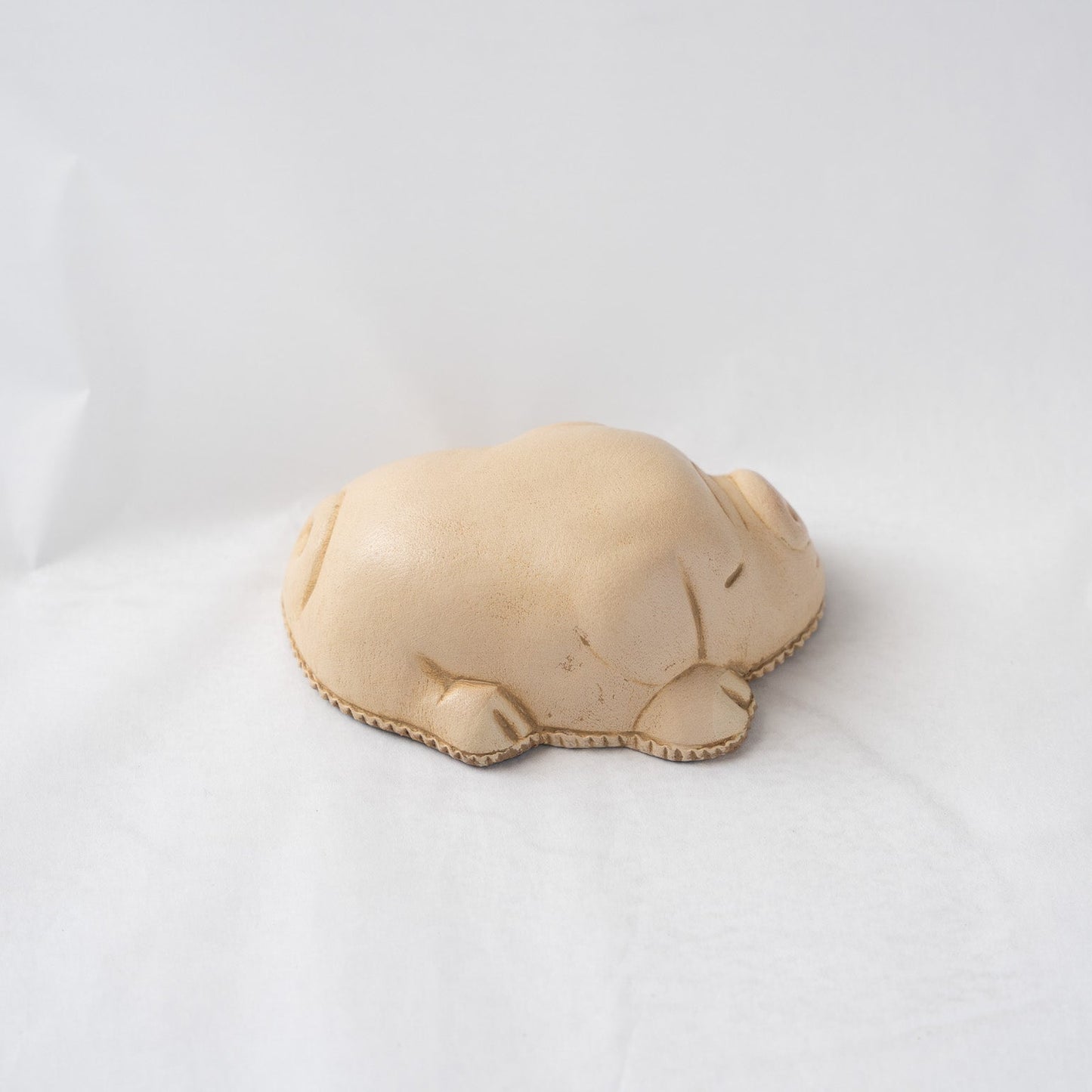 Right side view of the beige leather pig paperweight against a white backdrop, displaying the minimalist curves and soft shadow lines along its flank.