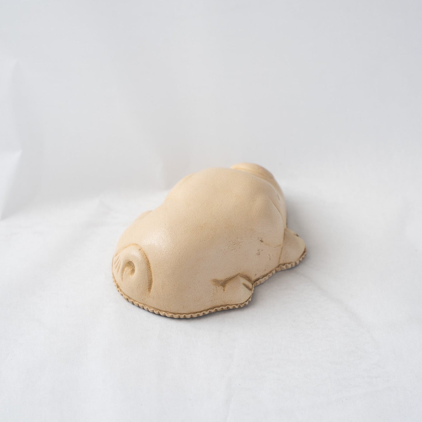 Right side view of the beige leather pig paperweight against a white backdrop, displaying the minimalist curves and soft shadow lines along its flank.