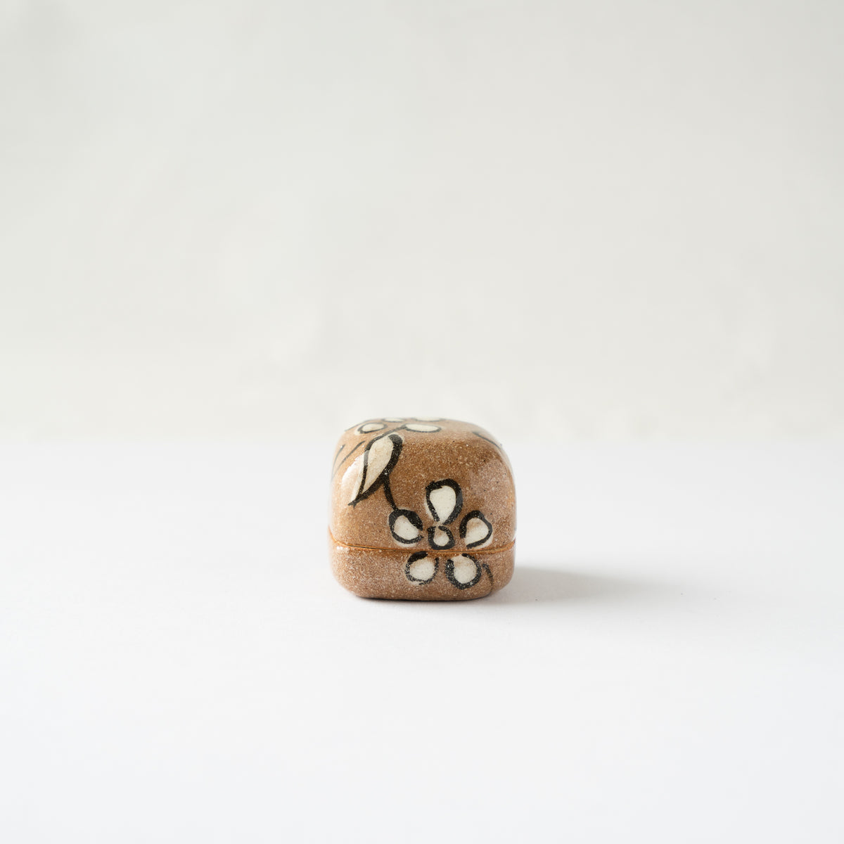 Turned side view of the Oribe miniature KOGO incense box, highlighting a painted four-petal white blossom with dark iron outline.