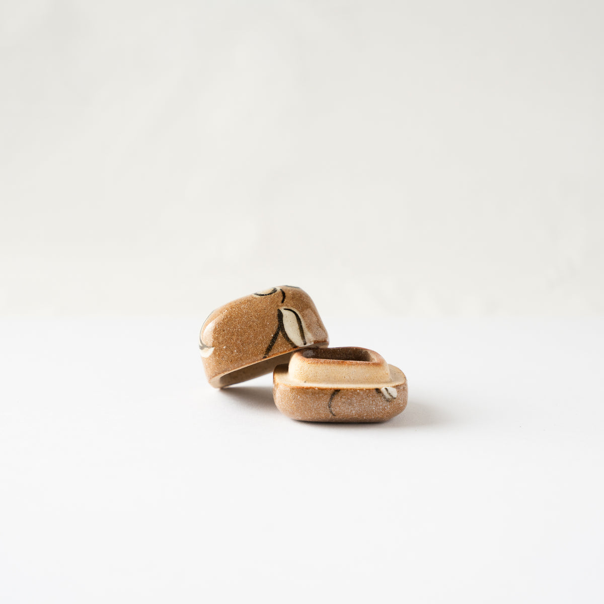Opposite low-angle view of the miniature Oribe KOGO container open, showing the smooth caramel glazed ceramic interior.