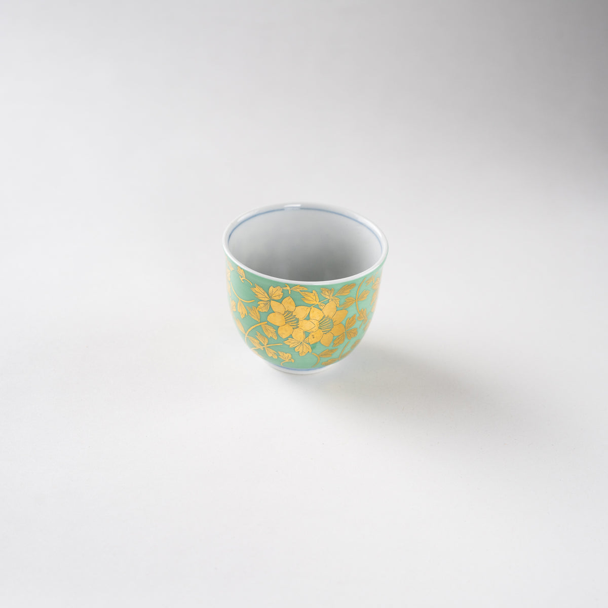 Tilted high-angle view of Mitsuru Yoshida's Kinrande sake cup, capturing the interior depth and the fine underglaze blue line on the rim.