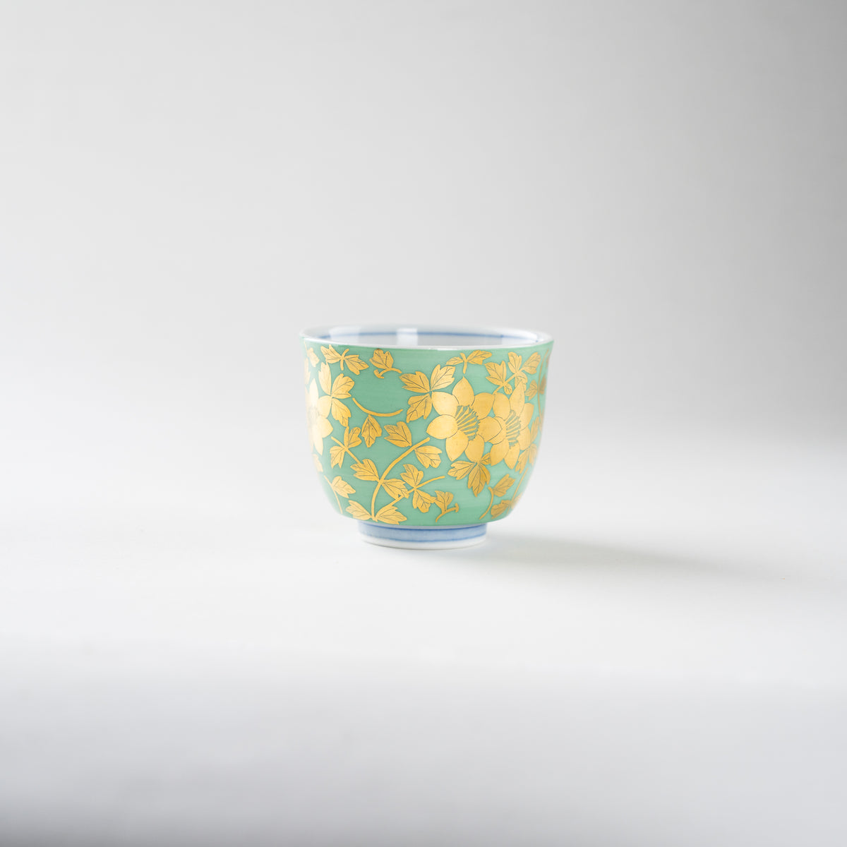 Side view of Mitsuru Yoshida's gilded floral GUINOMI sake cup, displaying the fine leaf details wrapping around the mint green exterior.