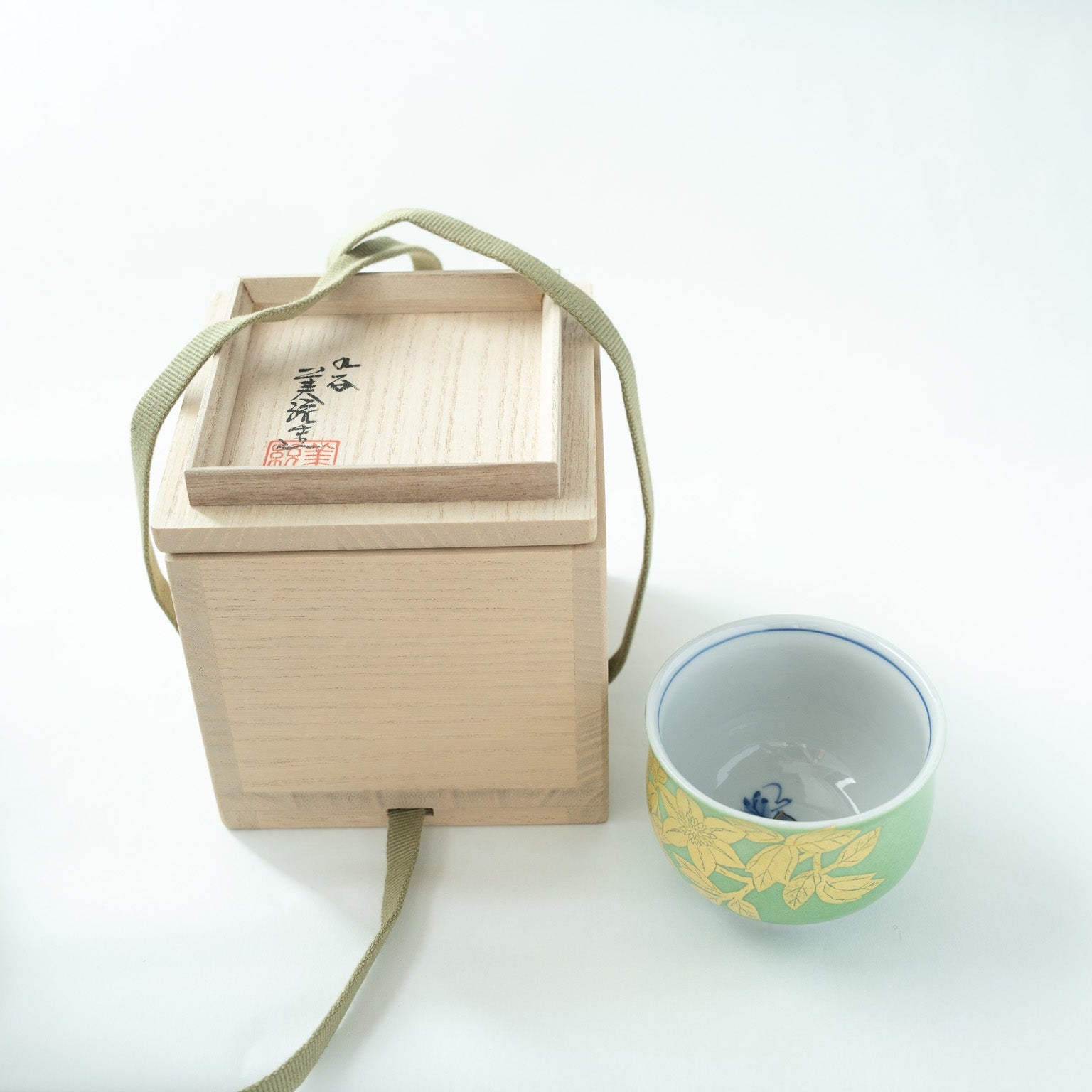 The Kutani Yuri-Kinsai GUINOMI shown next to its opened wooden box (tomobako), with the underside of the lid facing up to reveal the artist's handwritten signature and red seal.
