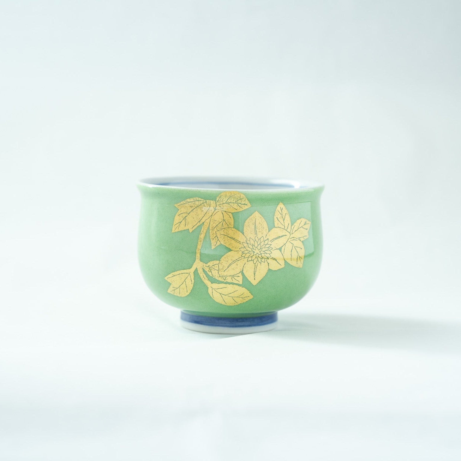Alternate side view of the GUINOMI, showcasing another cluster of masterfully applied gold leaf flowers against the smooth green background.
