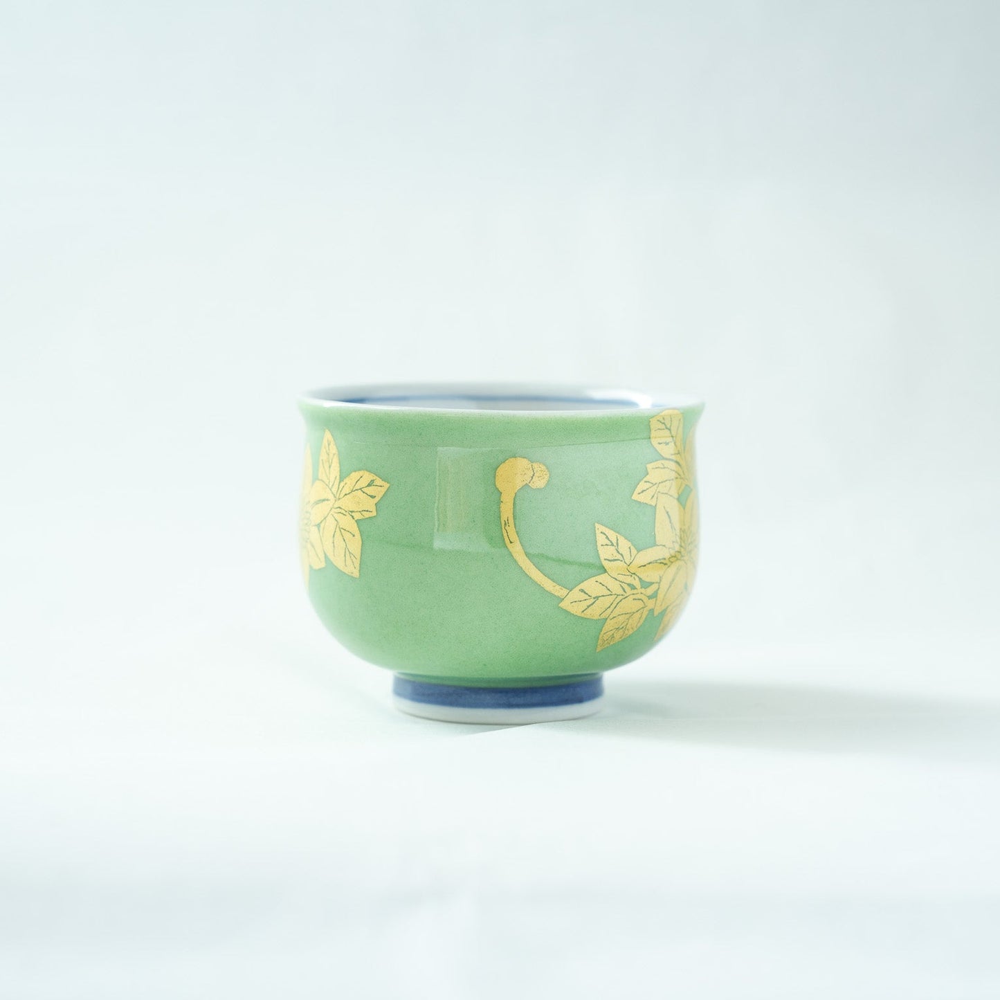 Profile view of the green Kutani sake cup, highlighting the elegant curvature and the continuation of the fine gold leaf stem and leaf design.