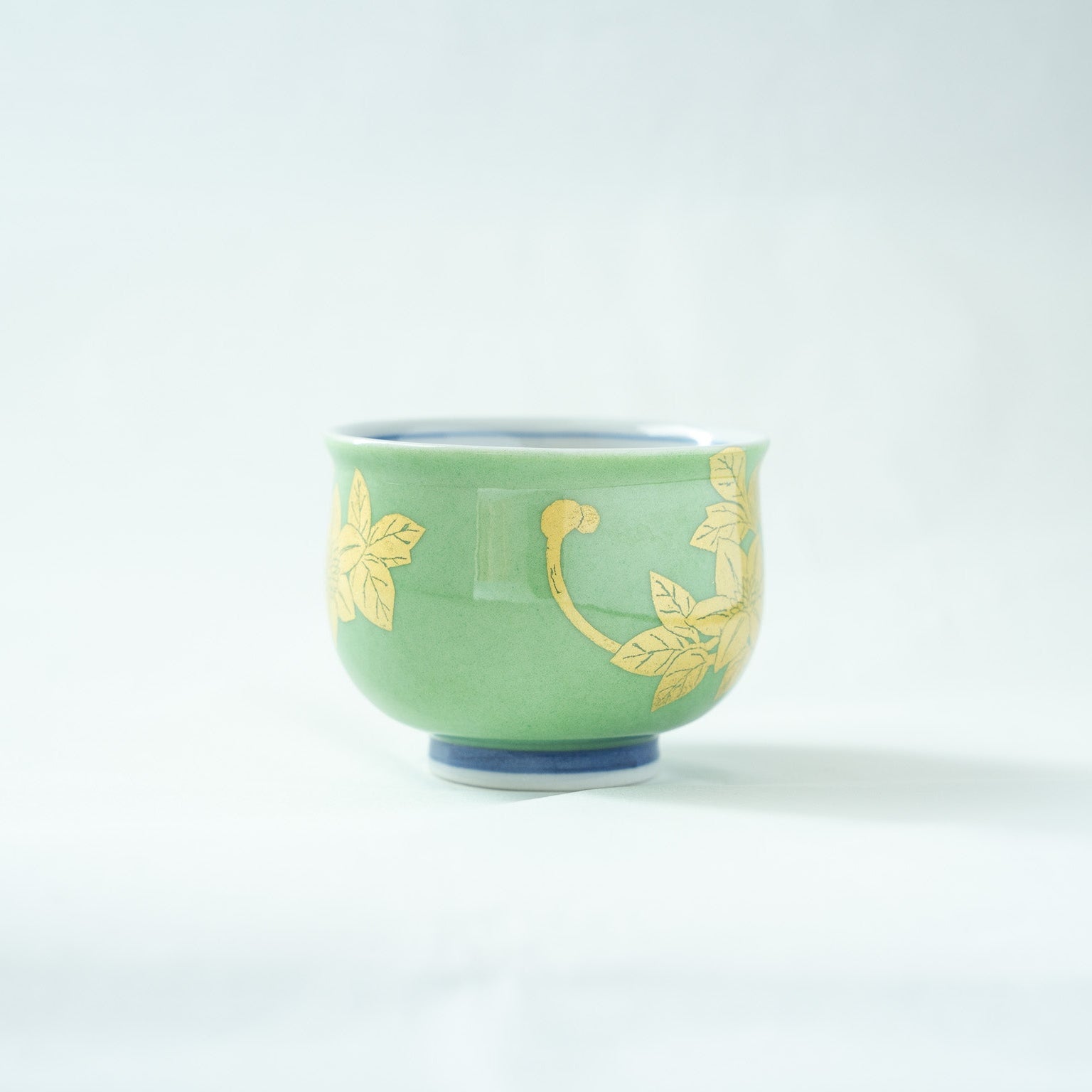 Profile view of the green Kutani sake cup, highlighting the elegant curvature and the continuation of the fine gold leaf stem and leaf design.