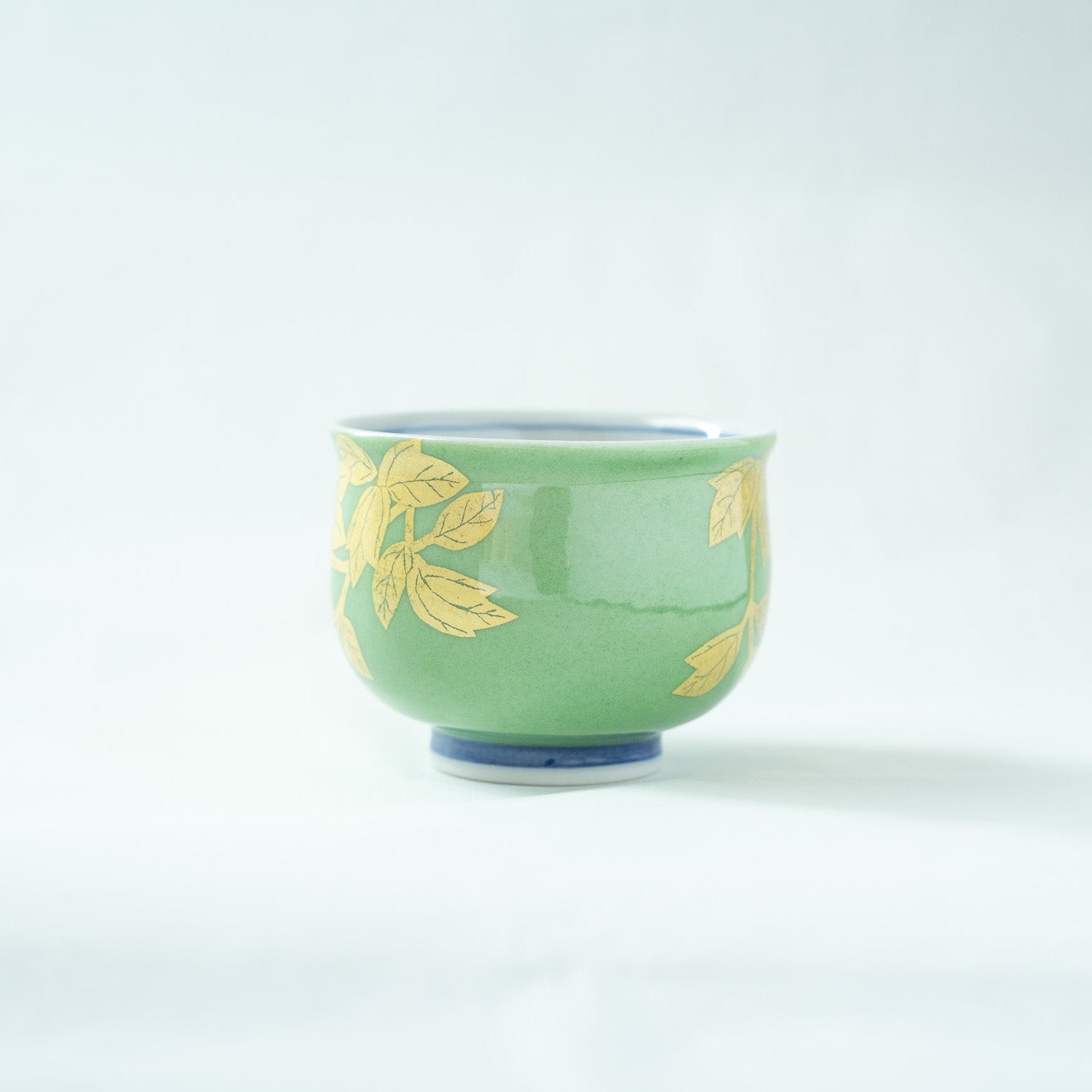 Back view of the vessel, capturing the solid soft green glazed surface with subtle gold foliage accents on the edges.