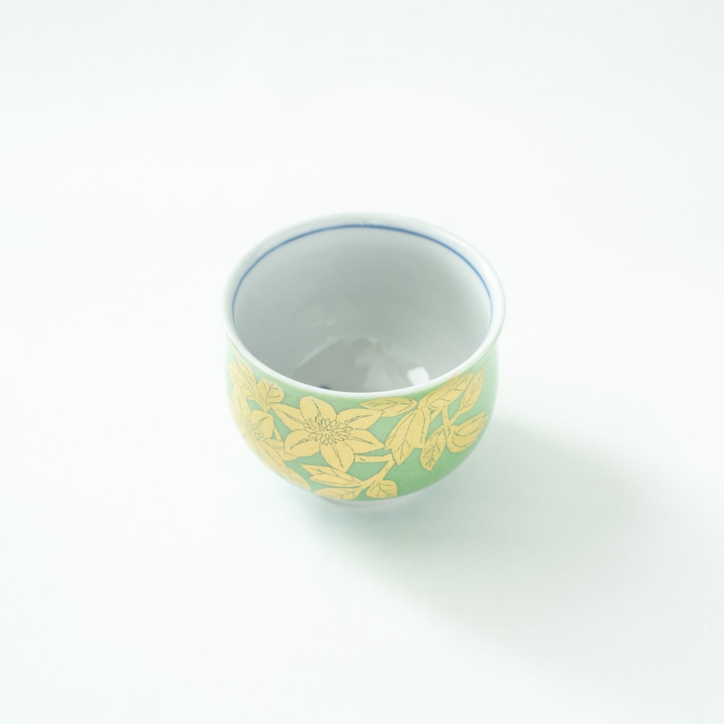 Top-down angled view looking inside the clean white porcelain interior of the GUINOMI, showing the blue rim accent line and gold exterior.
