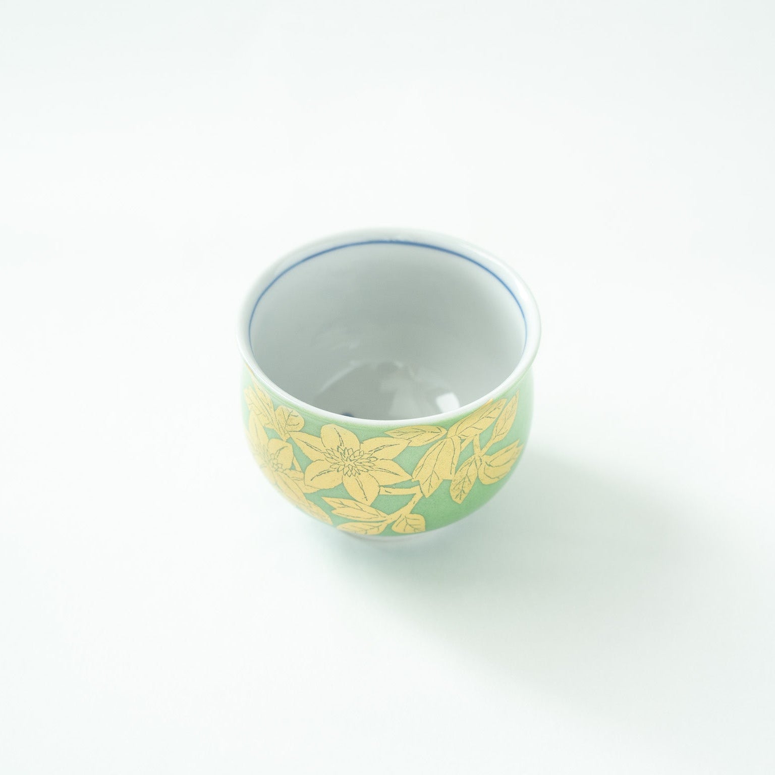 Top-down angled view looking inside the clean white porcelain interior of the GUINOMI, showing the blue rim accent line and gold exterior.