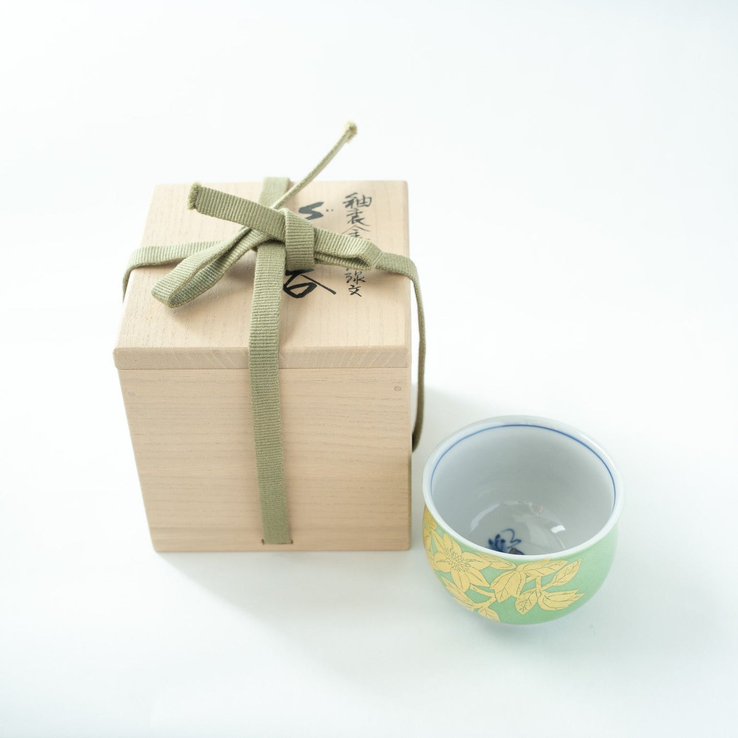 The green and gold Kutani GUINOMI presented beside its original signed paulownia wooden box tied with a green fabric ribbon.