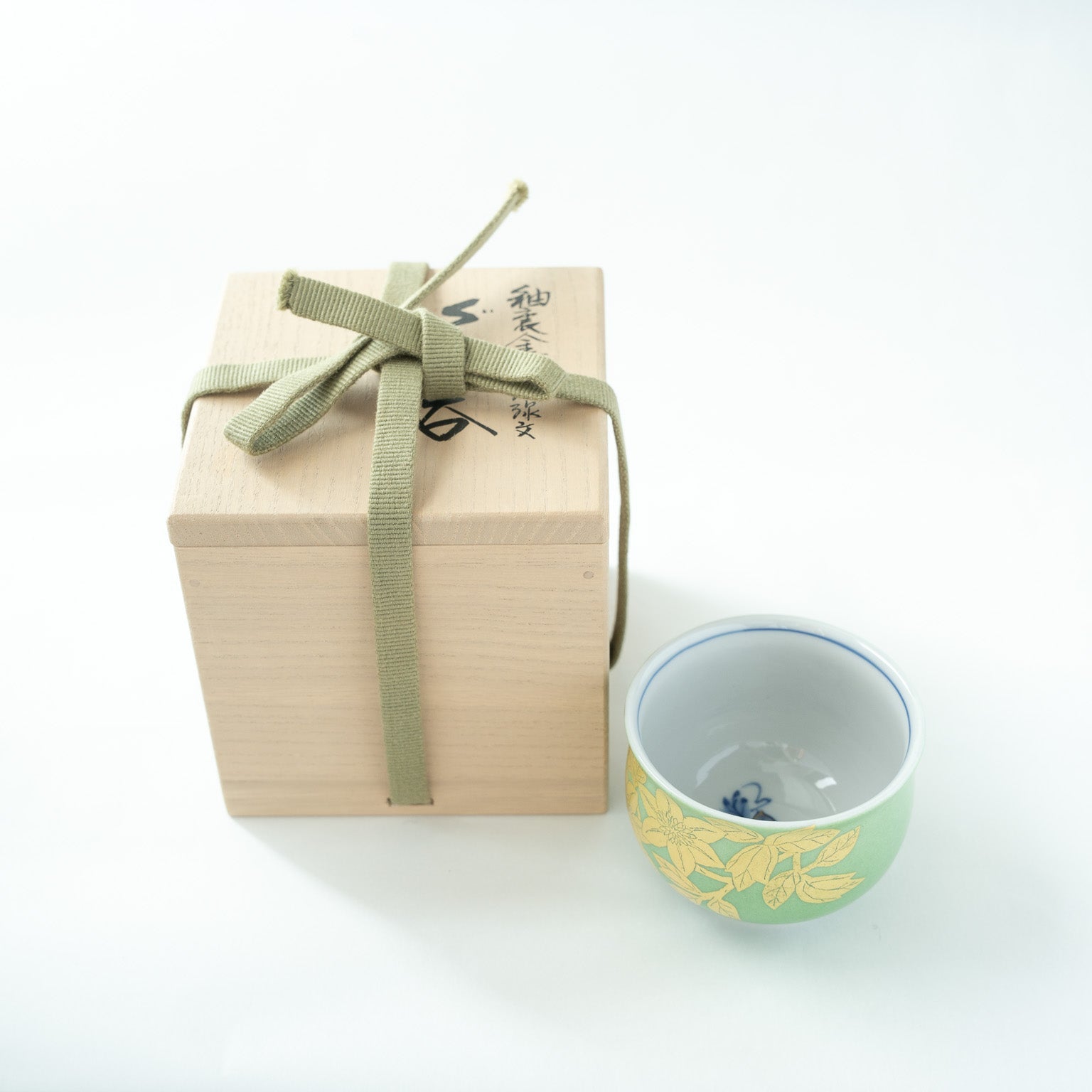 The green and gold Kutani GUINOMI presented beside its original signed paulownia wooden box tied with a green fabric ribbon.
