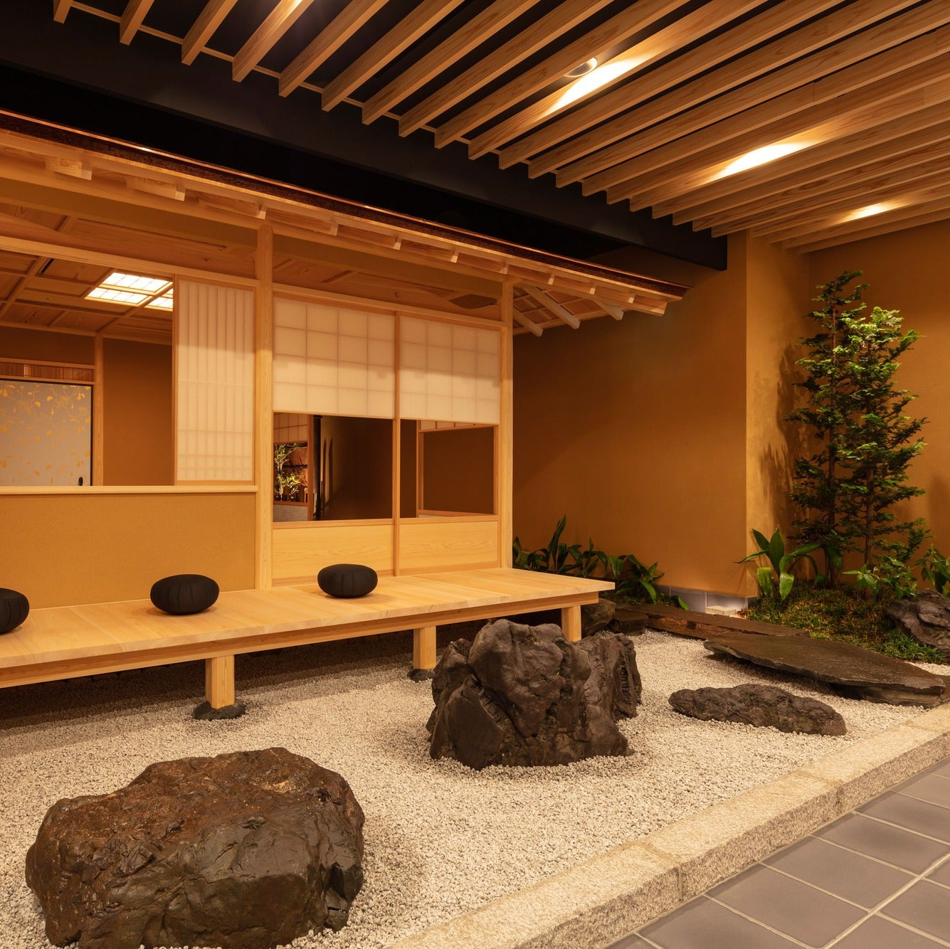 A long timber bench with round cushions faces a dry garden of rocks and raked gravel, a red curtain at the far end.