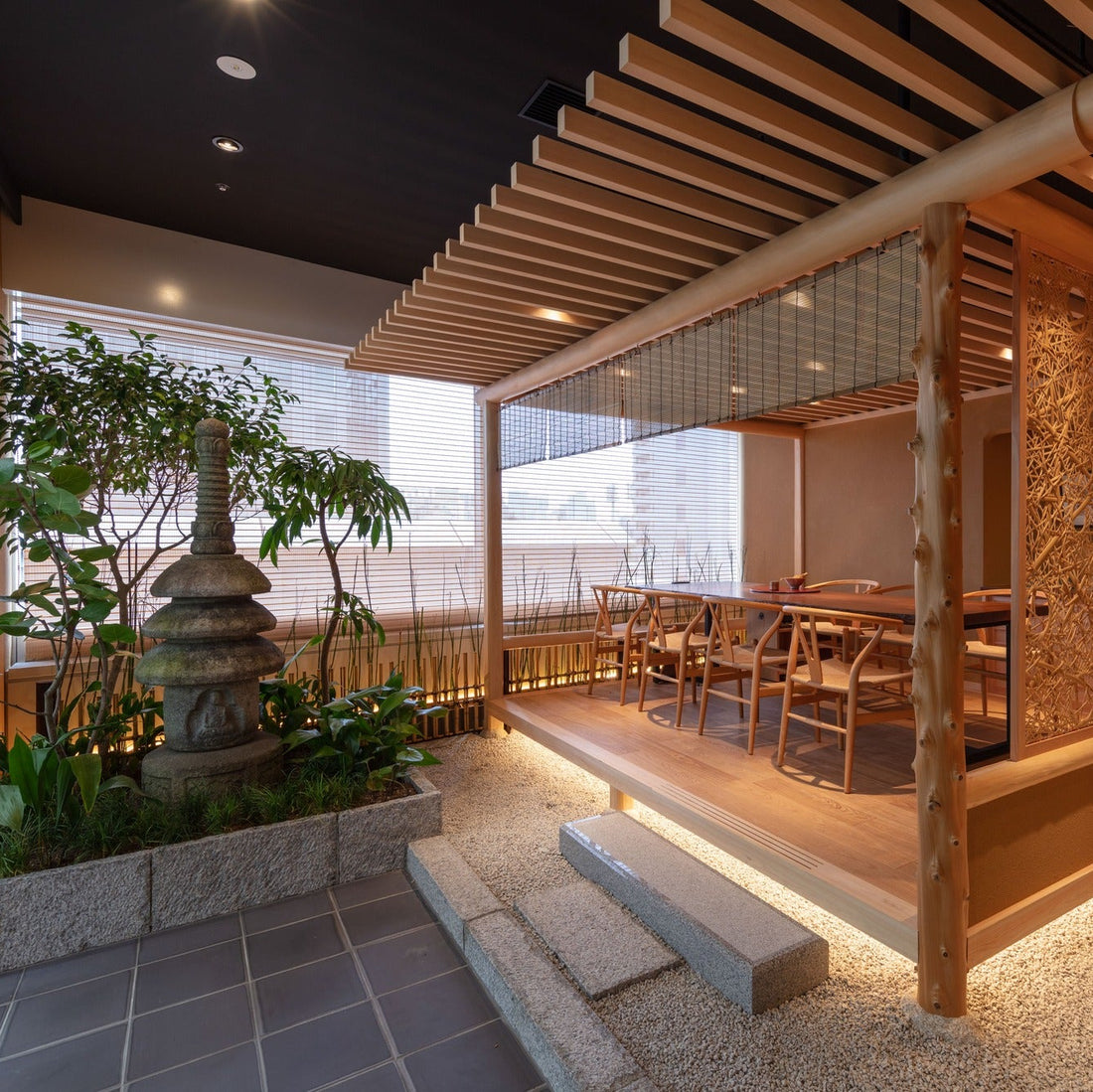 A planted courtyard with a stone pagoda meets a seating platform, the city faint beyond, work and garden in one Japanese office.