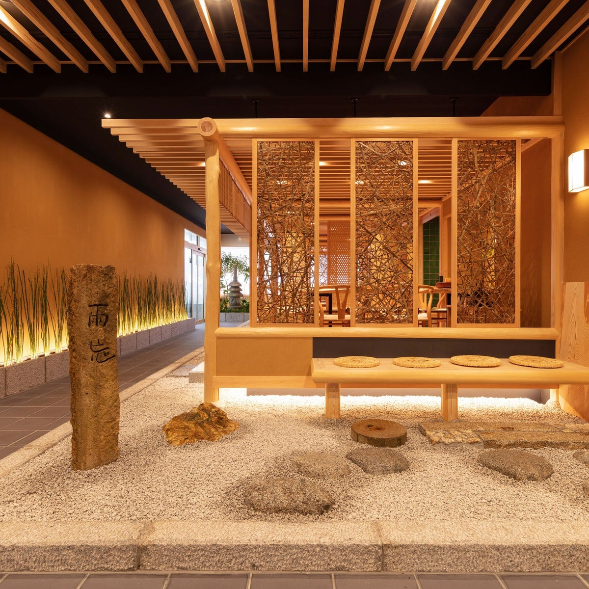 A raked gravel garden with a stone marker and a cushioned bench before woven screens, restrained Japanese architecture.