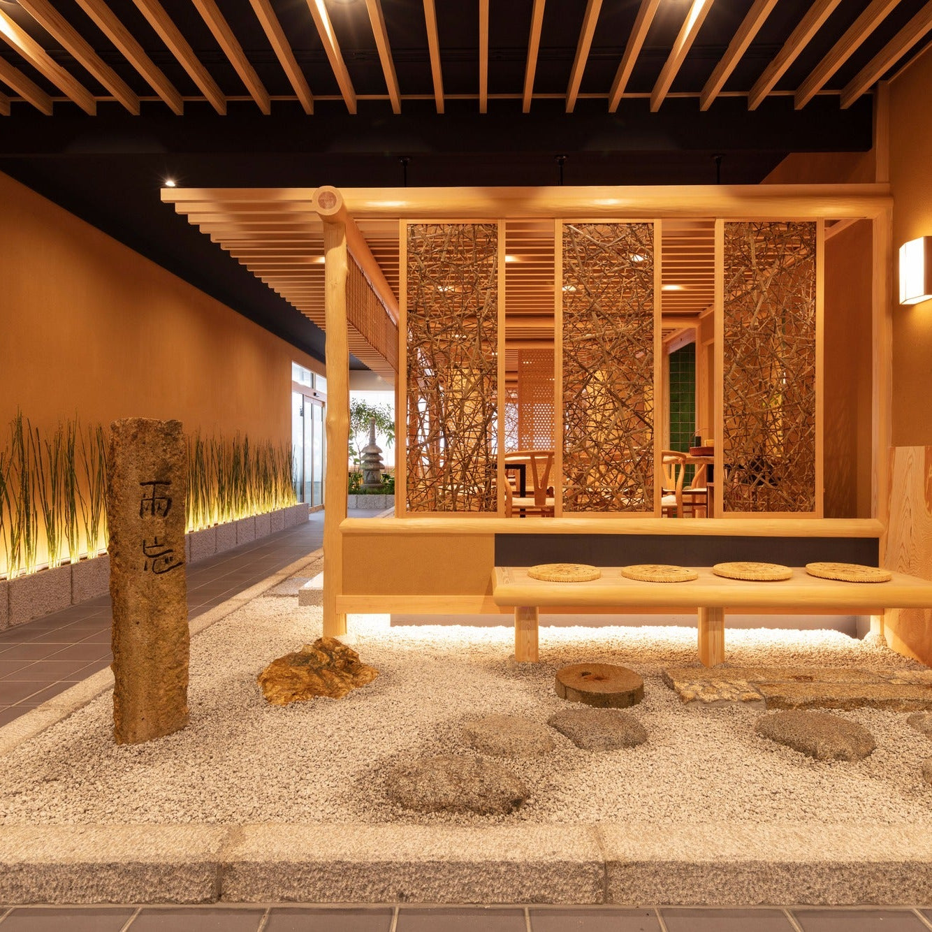 A raked gravel garden with a stone marker and a cushioned bench before woven screens, restrained Japanese architecture.