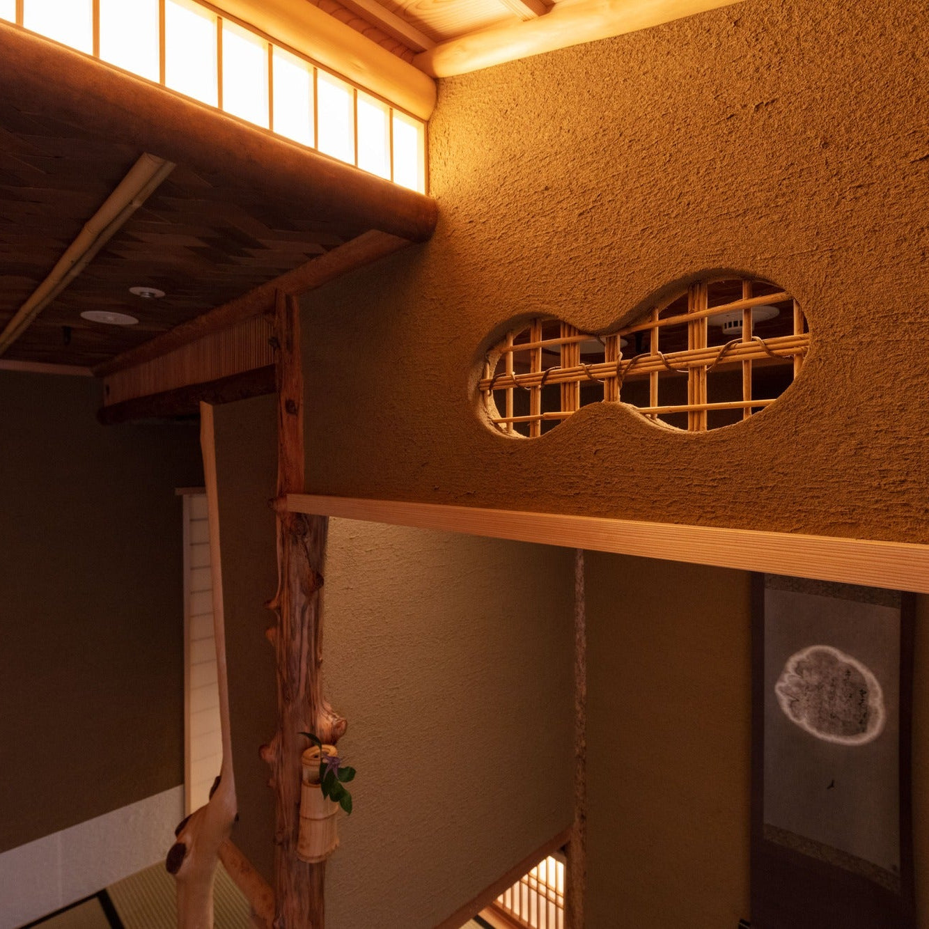 A gourd-shaped opening in an earthen wall reveals the bamboo lattice behind, beneath a woven bamboo ceiling.
