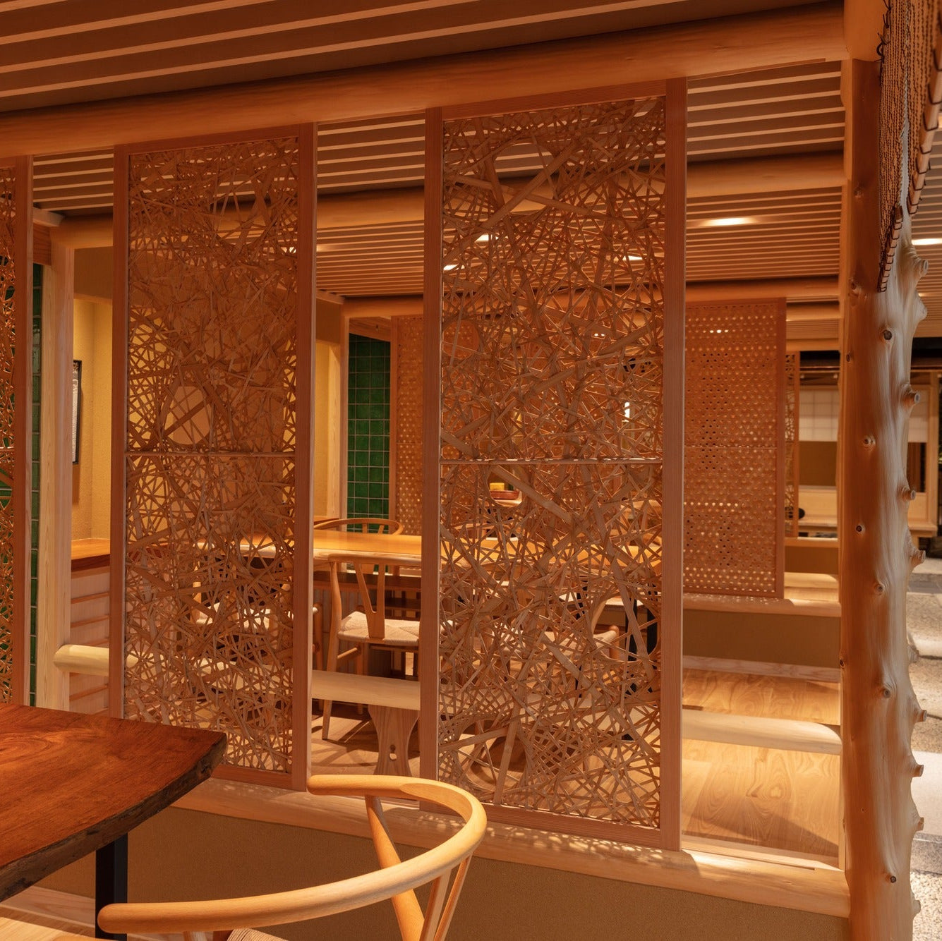 Three woven lattice panels stand open before a timber table, a natural post rising at the right.