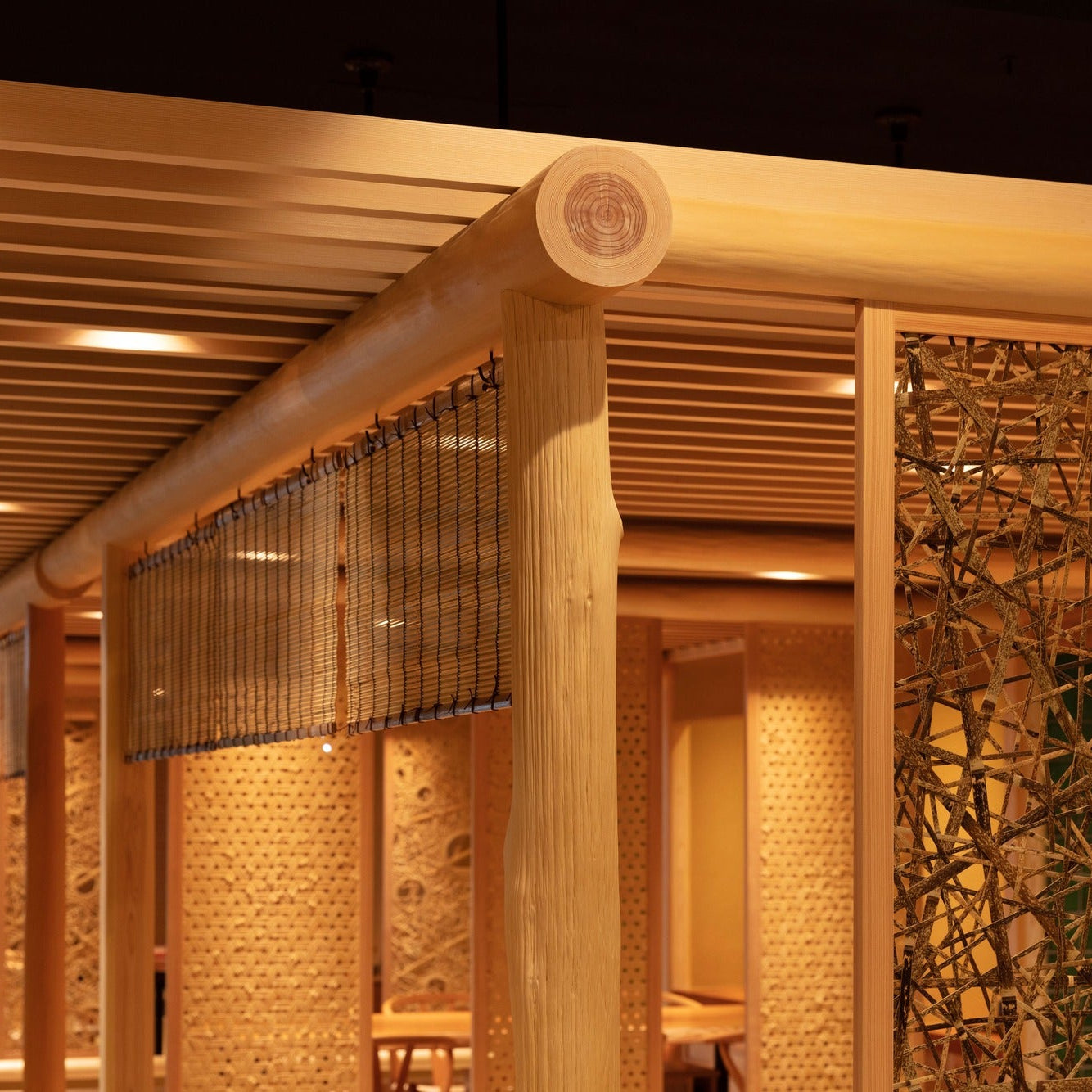 The cut end of a timber log post meets a beam above woven panels, a joint detail of Japanese architecture.